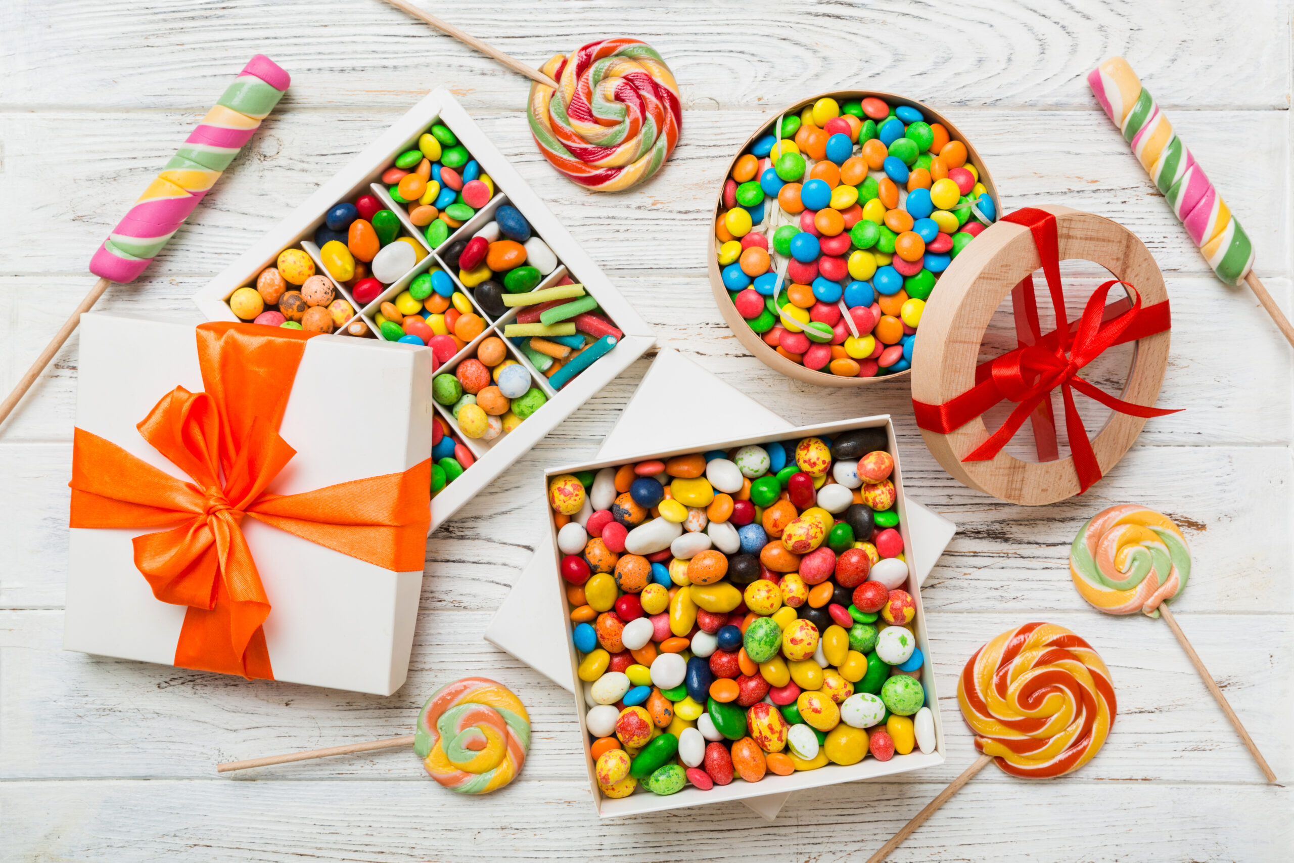 Set of different sweet candy in a paper box with a satin ribbon on a colored background. Holiday concept.